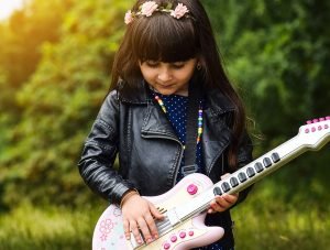 Little girl standing outside playing a small guitar - Adventures in NanaLand - Things to do with grandkids