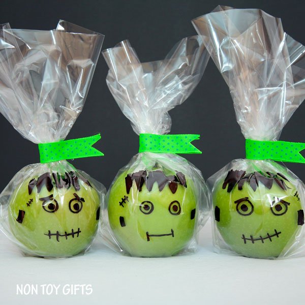 Green apples wrapped in cellophane with Frankenstein faces drawn on the bag in front of the apple - Non Toy Gifts